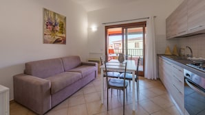 Una sala de estar con sofá, una mesa de comedor con sillas, una cocina con armarios y un balcón con vistas.