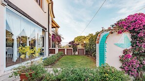 A residential property with a well-maintained garden, a balcony with a white railing, and a tiled wall with a geometric pattern.