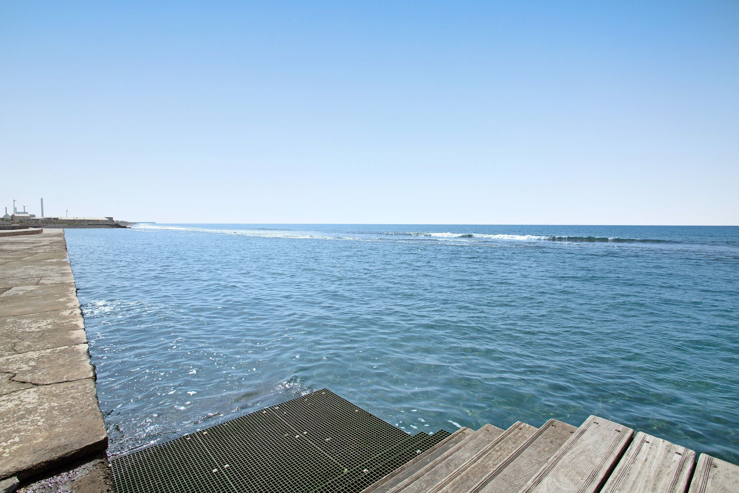 Eine Pier, die sich in ruhiges Wasser erstreckt, mit wolkenlosem Himmel darüber.