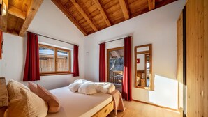 A bedroom with a wooden ceiling, a bed with pillows, a window with red curtains, and a mirror on the wall.