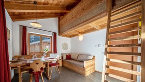 A cozy room with a wooden bench, a dining table with chairs, and a window with curtains.