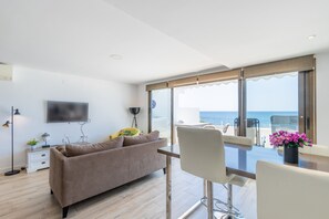 En moderne stue med sofa, fjernsyn, bord og havudsigt.