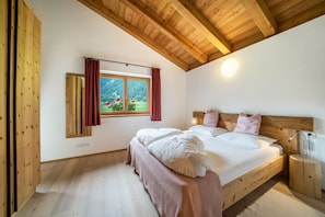 Un dormitorio con techo de madera, un ventanal con cortinas, una cama con almohadas y una mesita de noche.