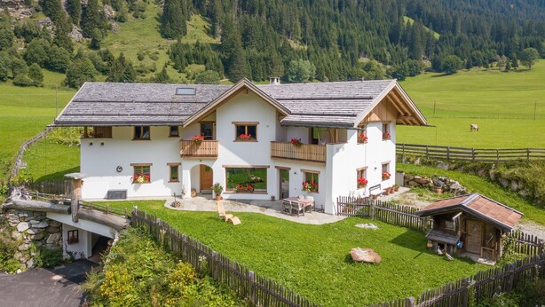 A two-story chalet with a balcony, a stone bridge, and a fenced yard. - Holiday Apartment "Larch Soge Apt Helmuth" with Mountain View, Balcony & Shared Garden (Racines)