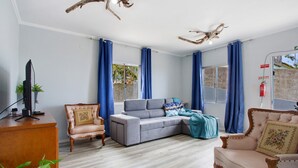 Een woonkamer met een bank, twee fauteuils, een houten bureau en een televisie.