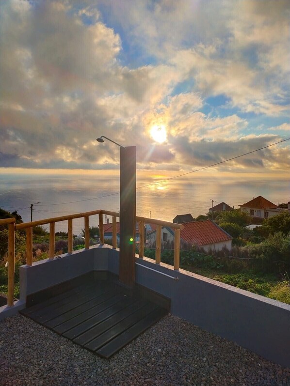 A wooden deck with a metal railing, a concrete platform, and a view of the sea and houses in the background.