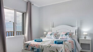 Een slaapkamer met een bed, nachtkastjes, een raam met gordijnen en uitzicht.