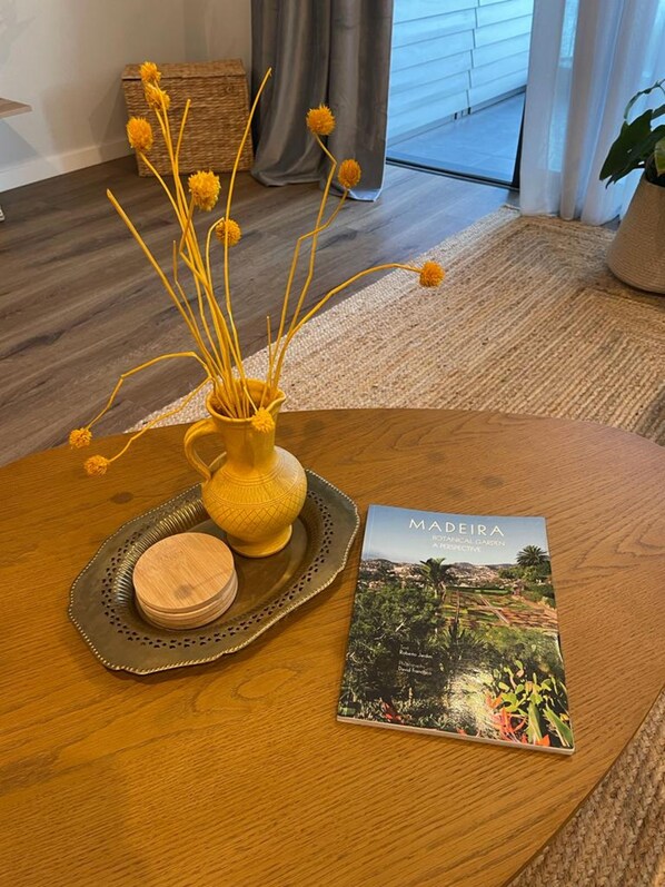 A wooden table with a yellow vase, a book titled 'MADEIRA Botanical Garden,' and a woven basket.