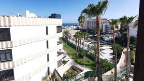 A multi-story building with balconies, a clear view of the sea, and palm trees.
