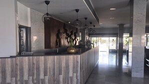 A reception area with a wooden reception desk, pendant lighting, marble flooring, and large windows allowing natural light.