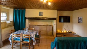 A cozy room with a wooden ceiling, a dining table with chairs, a kitchen area, and a television on the wall. - Country House with Large Garden, Family Room, and Pet-Friendly in Perigord (Montferrand-du-Périgord)