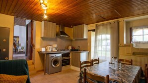 A compact kitchen with a washing machine, a dining table with chairs, and a wooden ceiling. - Country House with Large Garden, Family Room, and Pet-Friendly in Perigord (Montferrand-du-Périgord)
