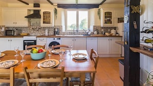A spacious kitchen with white cabinets, a wooden dining table set for four, and a black wooden column with wine bottles.