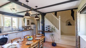 A dining area with a wooden table set for four, a blue bowl of fruit, and a potted plant.