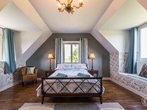 A bedroom with a sloped ceiling, a wooden bed, two bedside lamps, a window with curtains, and a patterned wall.