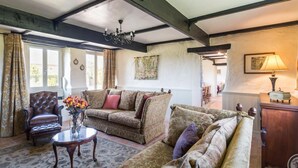 A traditional living room with exposed wooden beams, a sofa set, a leather armchair, and a chandelier.
