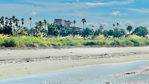 Ein Strand mit klarem Wasser, sandigem Ufer und einem Gebäude im Hintergrund.