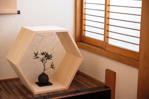 A minimalist wooden structure sits on a table near a window with a wooden frame.