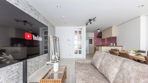 A modern living room with a large flat-screen TV, a stone-textured wall, a wooden coffee table, and a beige sofa. - Precious House Nipponbashi (Osaka)