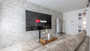 A modern living room with a stone-textured wall, a flat-screen TV mounted above a wooden coffee table, and a beige sofa. - Precious House Nipponbashi (Osaka)