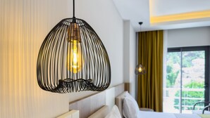 A modern hotel room with a unique wireframe pendant light, a large window with a view of greenery, and a neatly arranged bed with white linens. - Dedeoğlu Port Hotel (Fethiye)