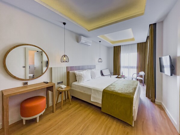 A hotel room with a bed, a desk, a chair, a small stool, a TV, and a window with curtains. - DedeoÄŸlu Port Hotel (Fethiye)