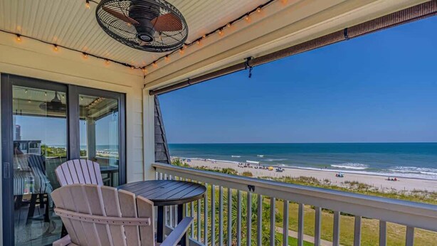 A balcony with a view of the beach, a fan, and a table with chairs. - Ocean Forest Villas C310 - Oceanfront (Myrtle Beach)