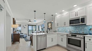 A modern kitchen with white cabinets, stainless steel appliances, and a blue mosaic backsplash. - Ocean Forest Villas C310 - Oceanfront (Myrtle Beach)