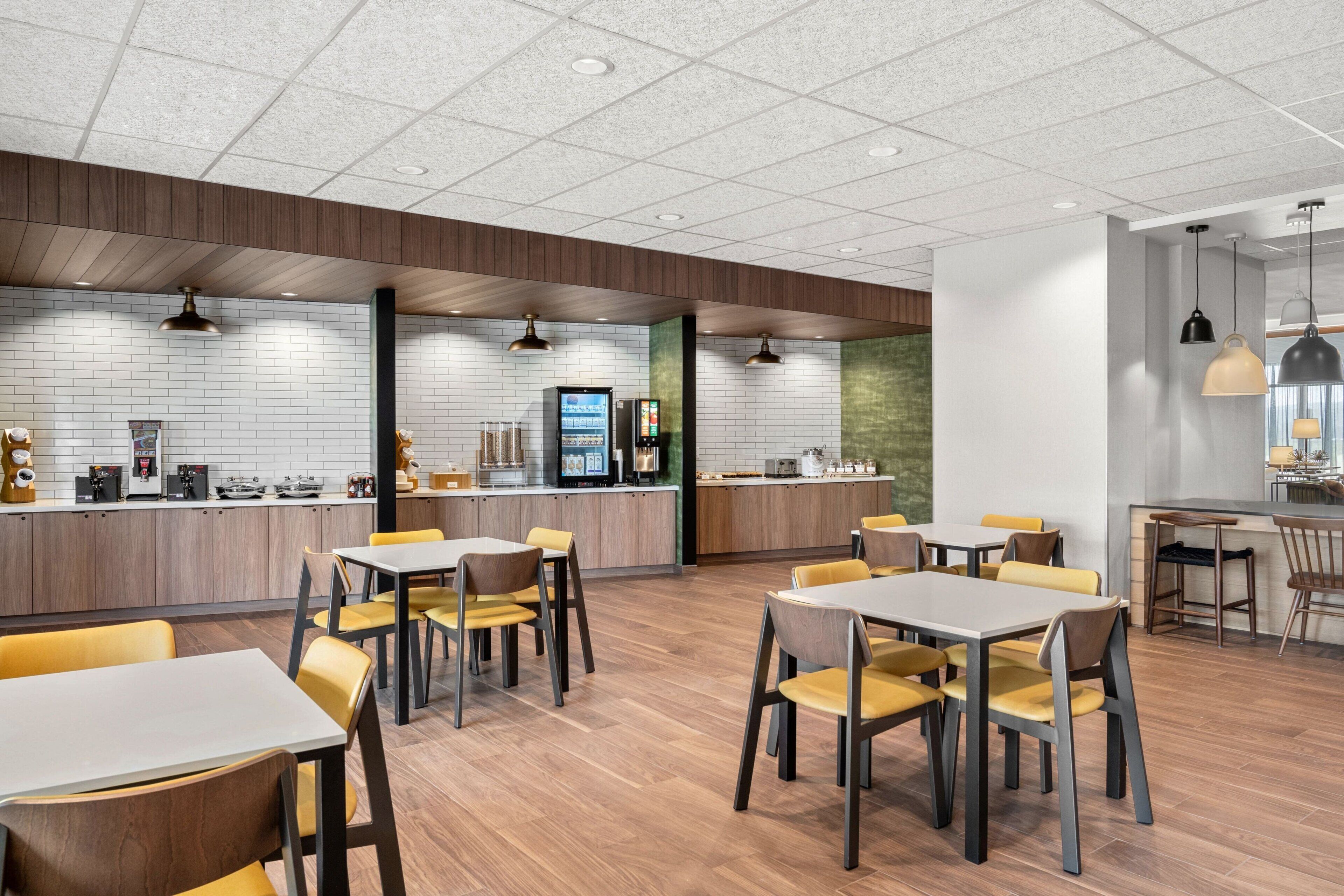 A modern restaurant with wooden flooring, yellow chairs, and a counter with a coffee machine.