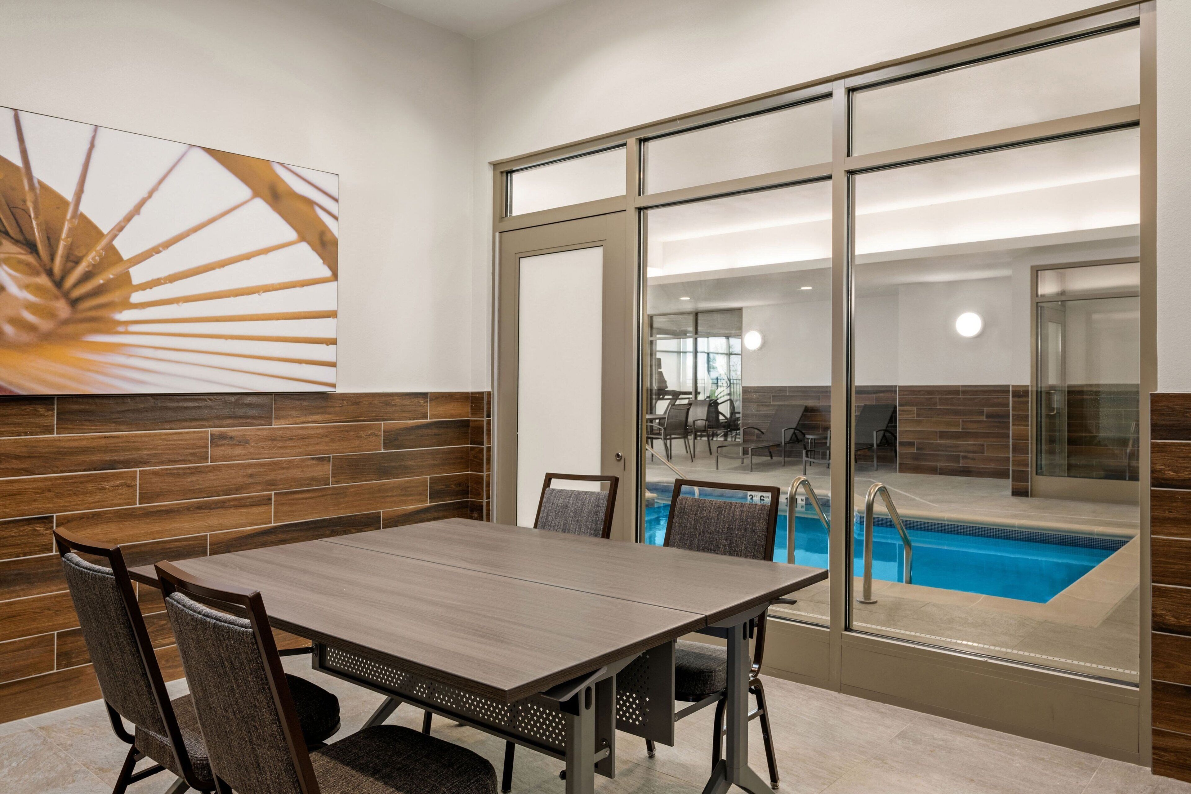 A conference room with a large table and chairs, a glass wall with a pool view, and a modern design with wooden accents.