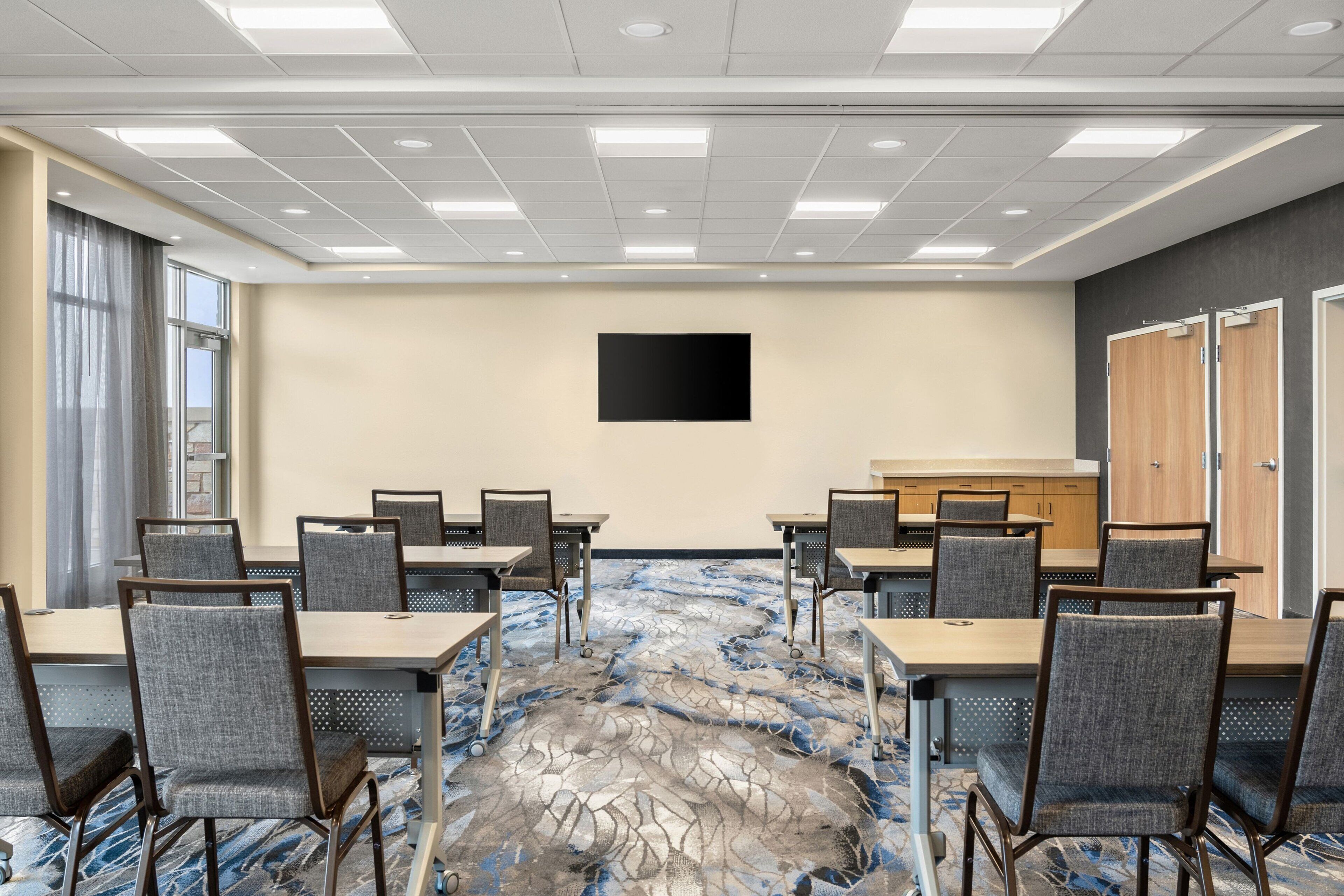 Un salón de conferencias con una mesa grande y sillas, un televisor de pantalla plana en la pared, y piso alfombrado.
