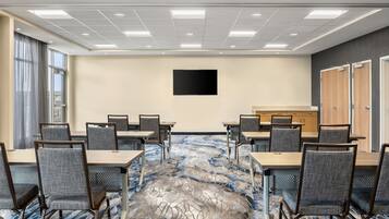 Un salón de conferencias con una mesa grande y sillas, un televisor de pantalla plana en la pared, y piso alfombrado.