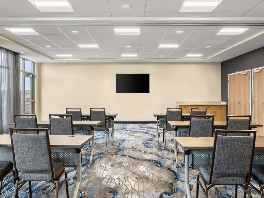Un salón de conferencias con una mesa grande y sillas, un televisor de pantalla plana en la pared, y piso alfombrado.