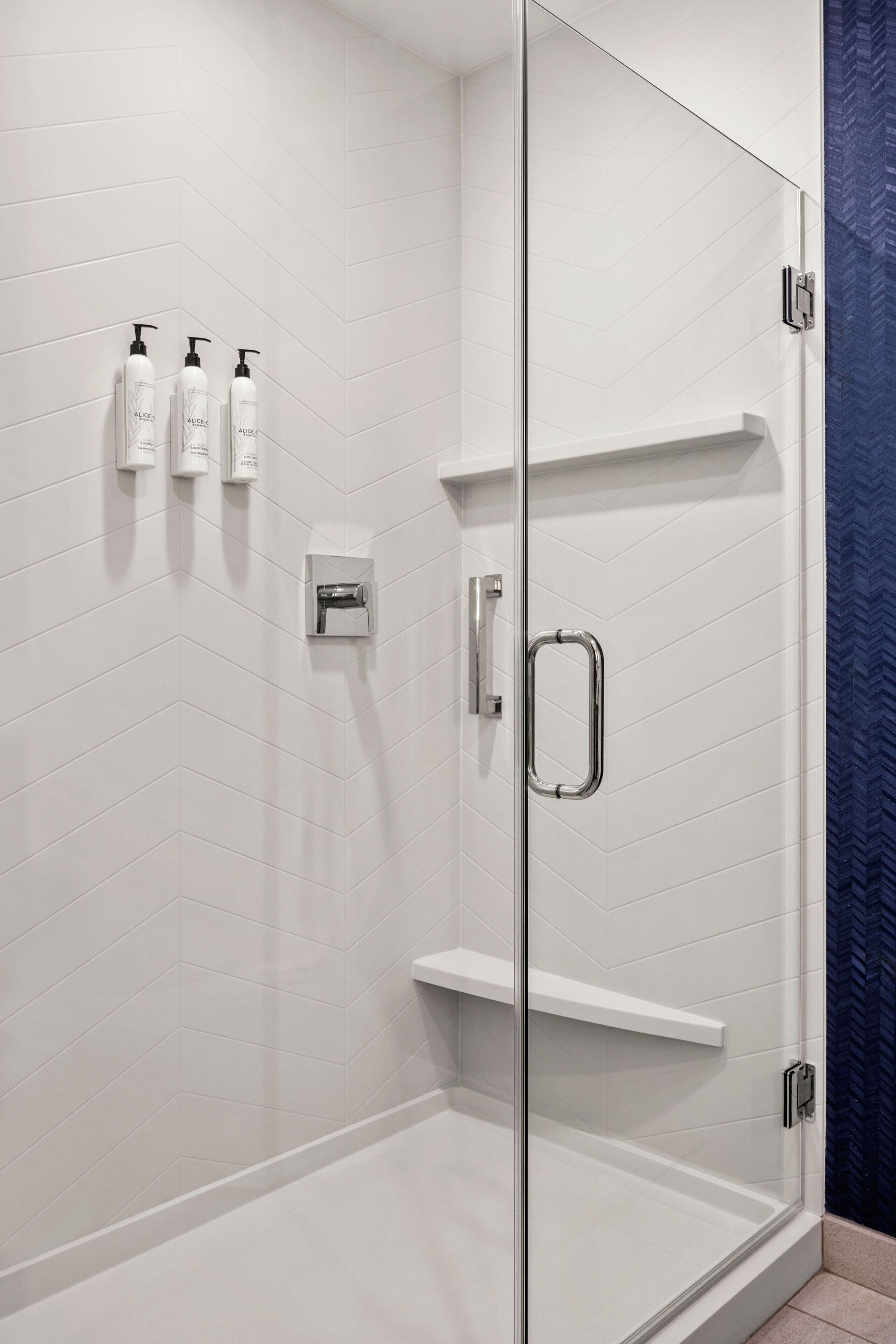Un área de ducha moderna con puertas de vidrio, paredes de azulejos blancos y una pared de acento azul.