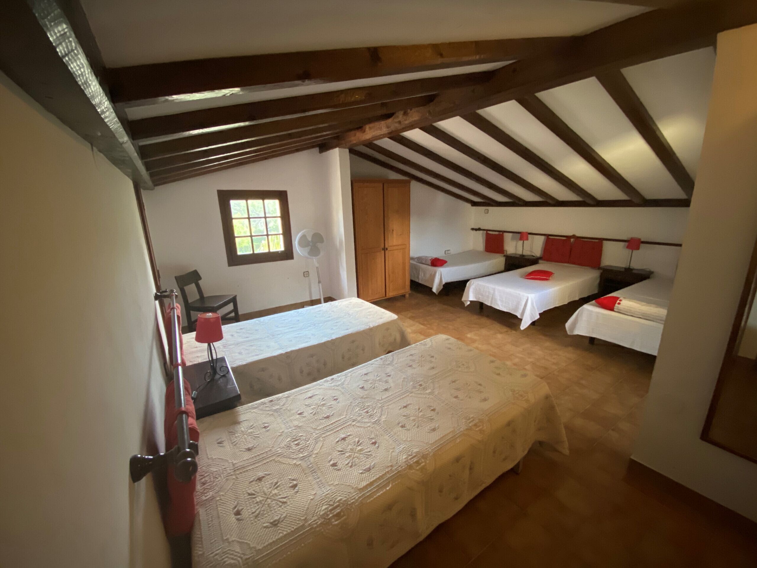 Une chambre avec deux lits simples, un plafond en bois, une petite fenêtre et un ventilateur.
