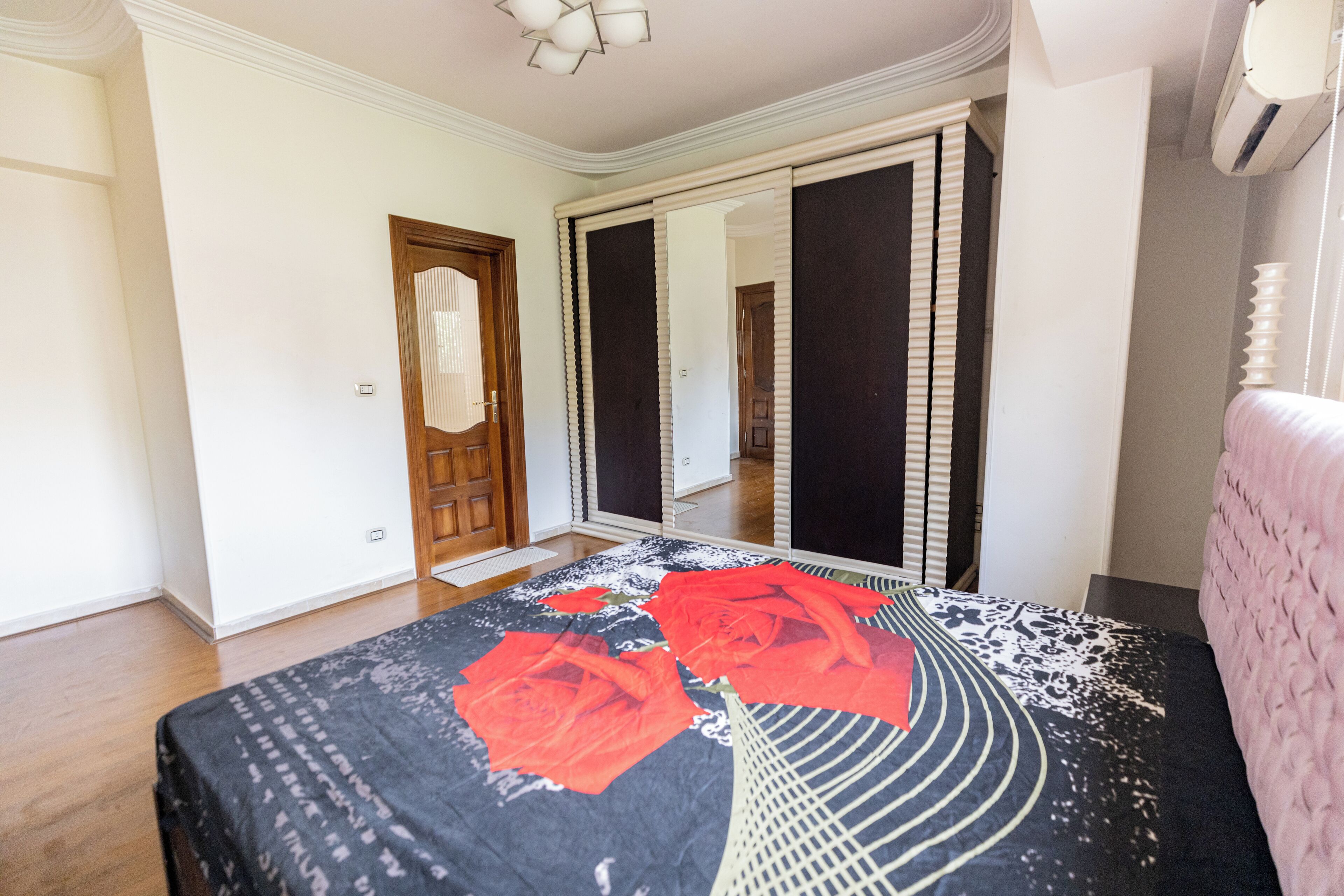 Un dormitorio con una cama, una puerta de madera, un espejo y una ventana.