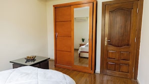 A bedroom with a bed, a wooden wardrobe, a small table with a bowl, and a wooden door. - Hibiscus Haven Suite  (Cairo)