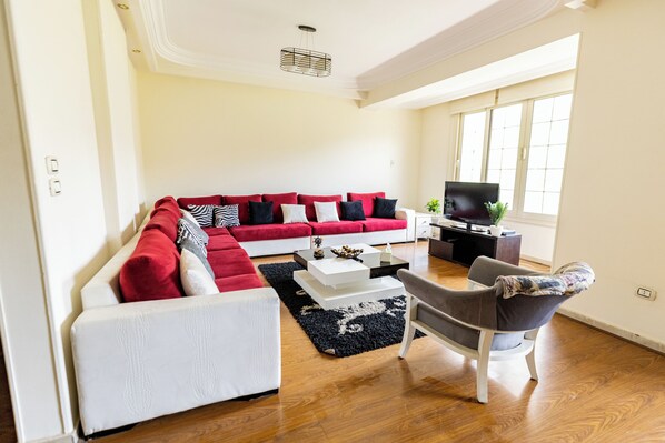 A modern living room with a red and white sectional sofa, a grey armchair, a coffee table, and a flat-screen TV.