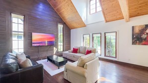 A spacious living room with a high ceiling and large windows, a flat-screen TV, and a fireplace. - Luxury Log Retreat, King Bed, Games Room (Bayfield)