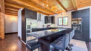 A modern kitchen with a central island, black cabinets, stainless steel appliances, and a wooden ceiling. - Luxury Log Retreat, King Bed, Games Room (Bayfield)