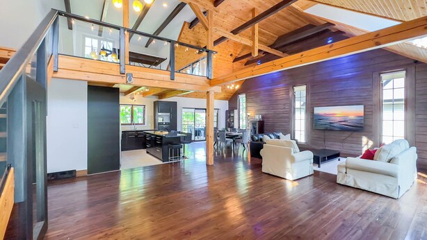 A spacious living area with a high ceiling, wooden beams, a kitchen, and a dining area. - Luxury Log Retreat, King Bed, Games Room (Bayfield)