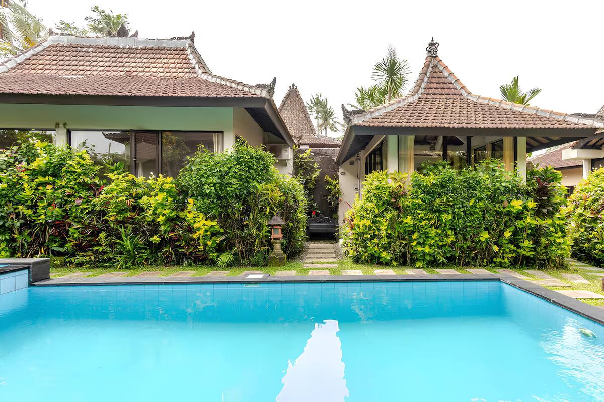A swimming pool surrounded by traditional buildings with tiled roofs and lush greenery.