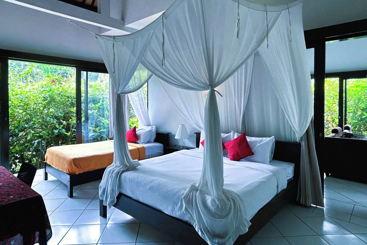 A bedroom with a canopy bed, two bedside tables, and a view of greenery outside.