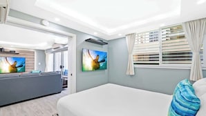Una habitación de hotel moderna con cama, sofá, televisor y ventana con persianas.