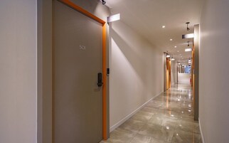 A modern hotel corridor with a clean, minimalist design, featuring a polished floor and bright lighting.