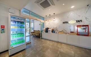 A hotel reception area with a vending machine, a sofa, a coffee machine, and a wall with the hotel's name.