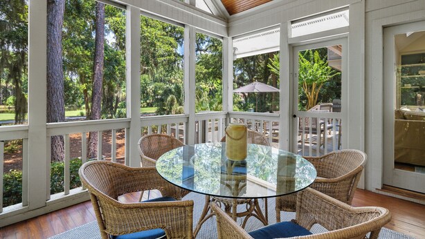 A covered patio with wicker furniture and a glass table, overlooking a lush garden. - Premier Golfside Getaway | Coastal Gallery (Kiawah Island)