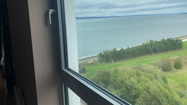 A view from a window overlooking a body of water with a distant shoreline and trees. - Modern 2 bed apartment with stunning seaside view (Leith)