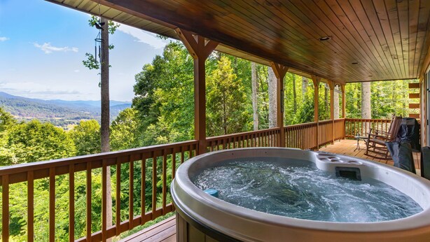 Un jacuzzi en una terraza de madera con vistas a un bosque y montañas.