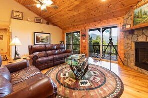 A cozy living room with a leather couch, a glass coffee table, and a fireplace. - On Mountain Time -Secluded 2 King BR, 2BA Log Cabin, HT, FP, VIEWS! (Waynesville)